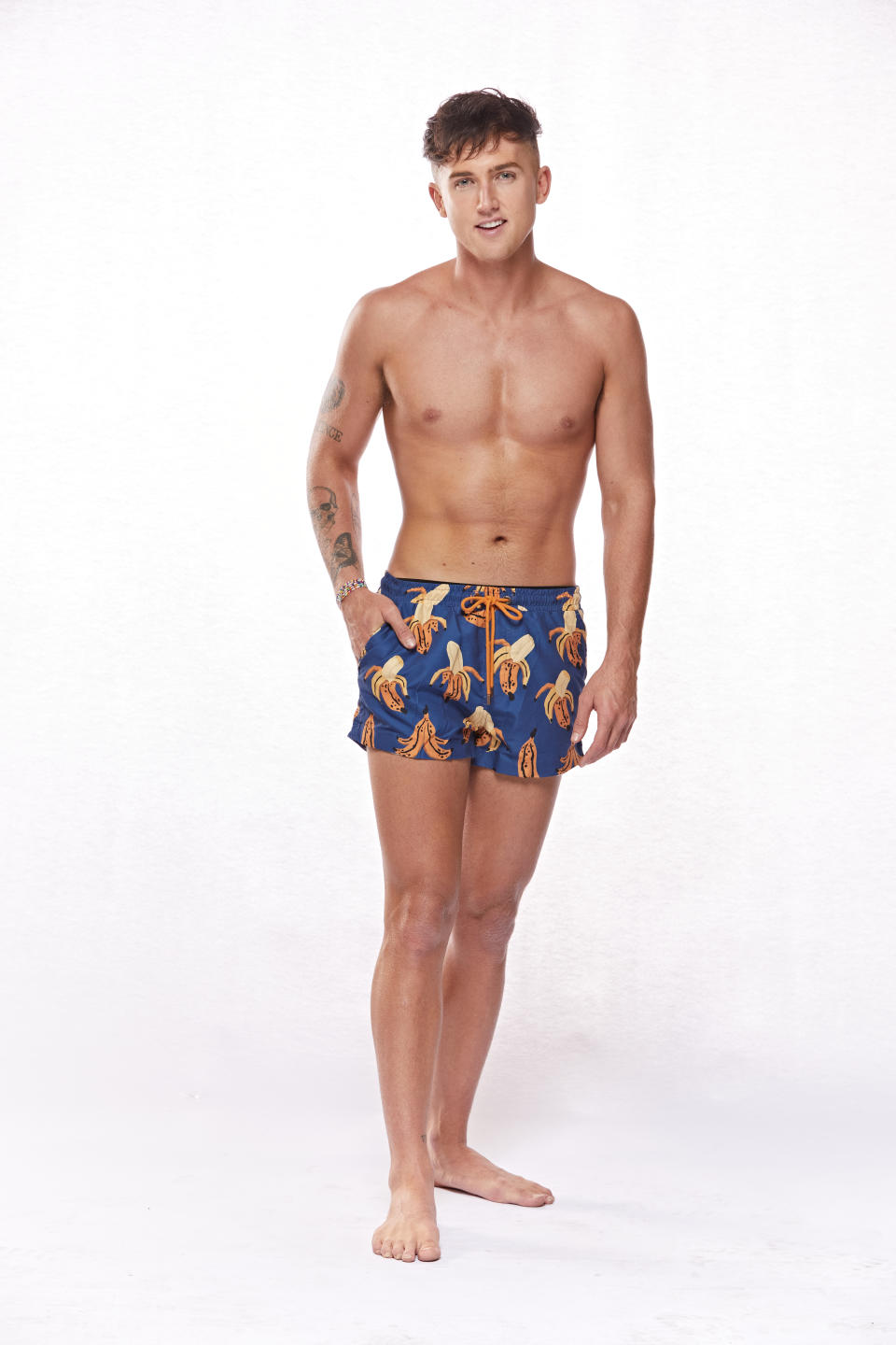 Contestant Mitchell stands smiling in board shorts against a white background