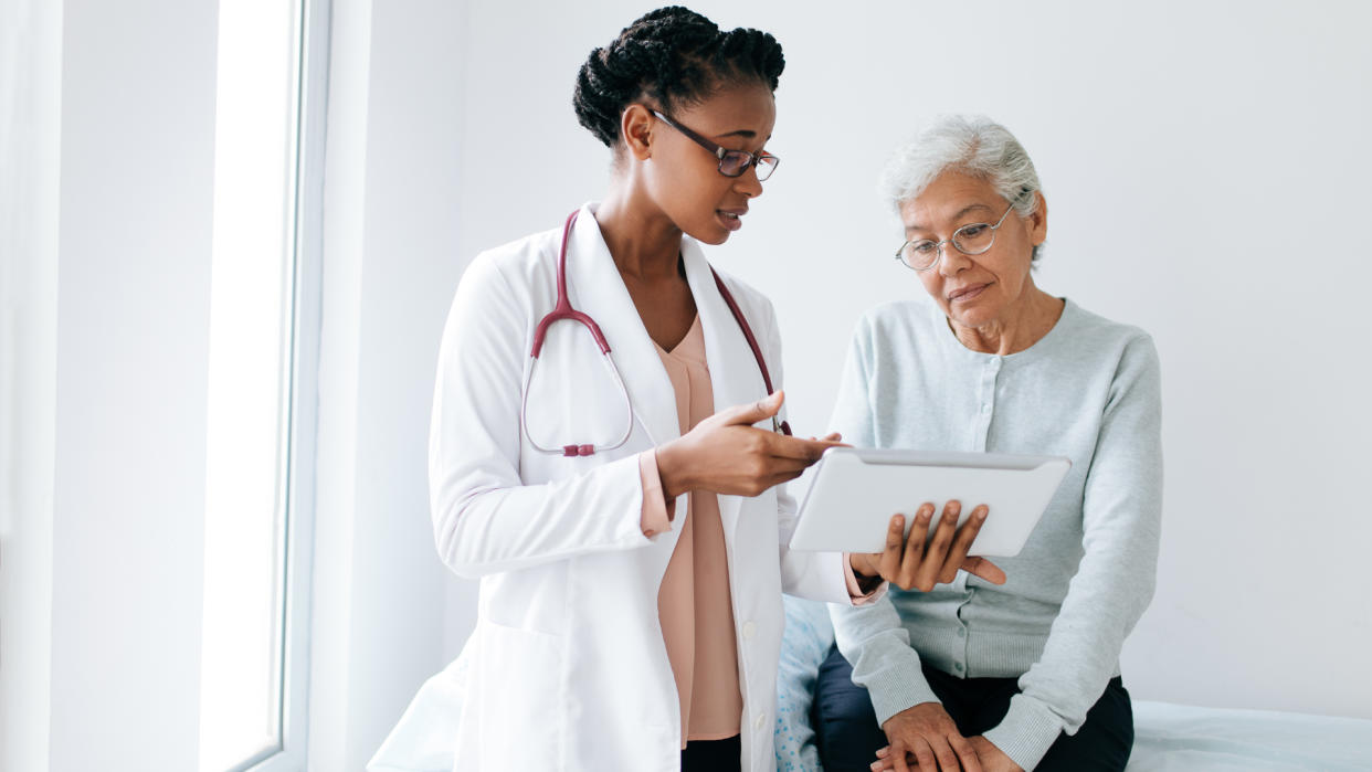 A black female doctor standing next to female patient and showing her something on digital tablet.