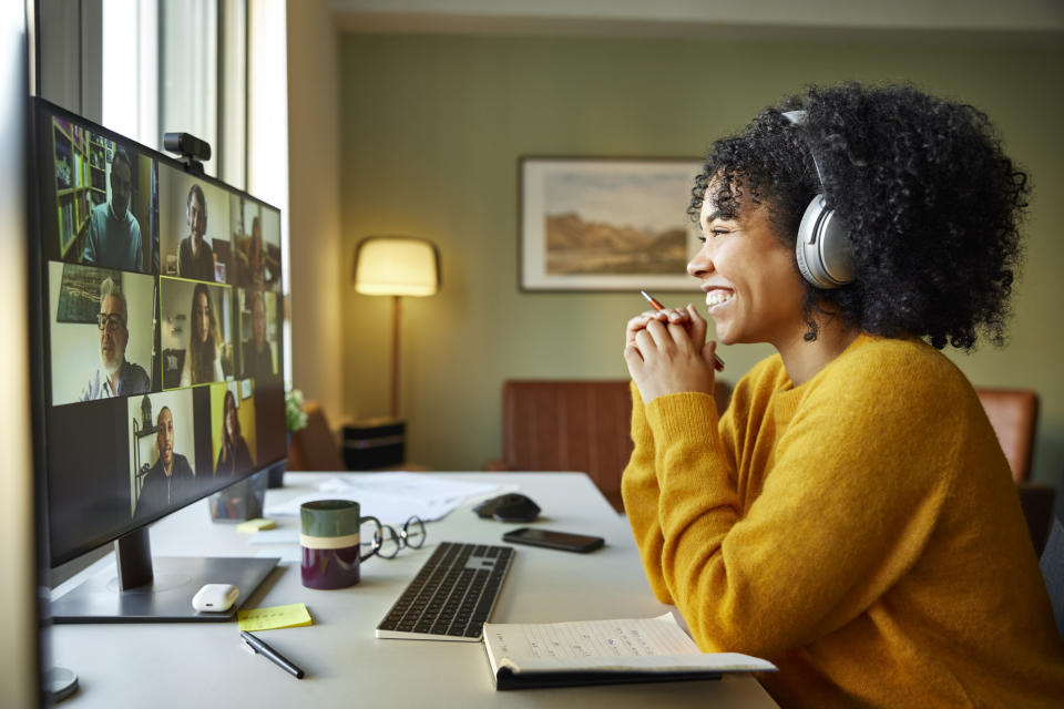 A person sits at their desk during a virtual meeting as they smile widely at their coworkers on the screen