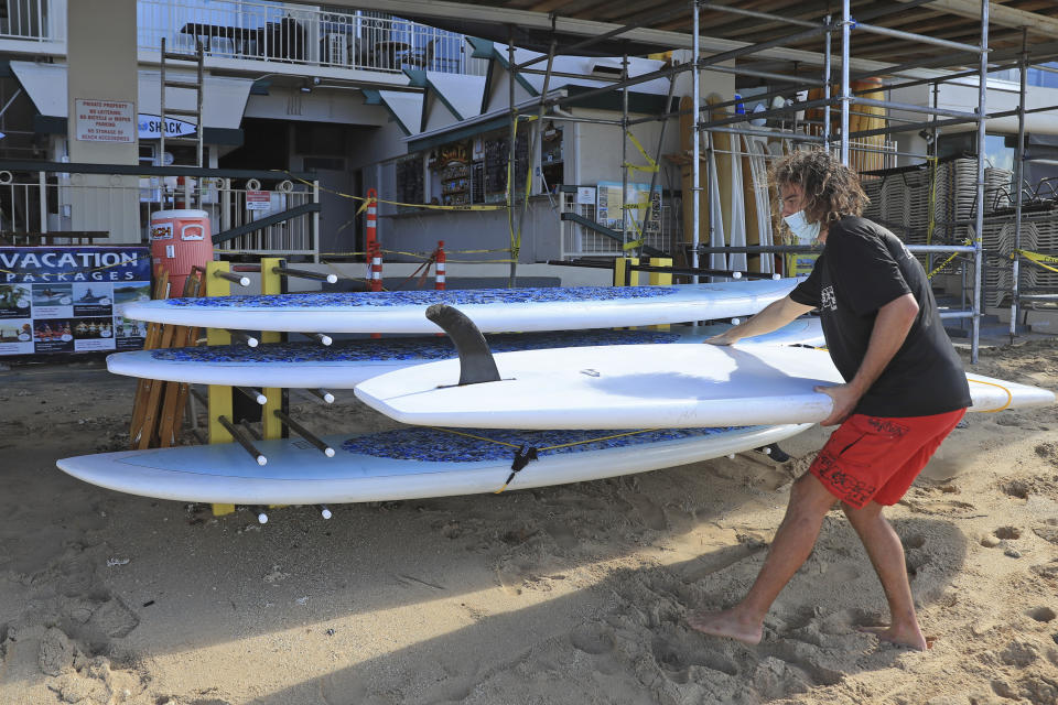Mitch Kemp, a worker at a Waikiki Beach rental company, readies a paddle board for rental Thursday, Oct. 15, 2020, in Honolulu. The beach rental company opened for the first time Thursday since closing in March due to the COVID-19 pandemic. A new pre-travel testing program will allow visitors who test negative for COVID-19 to come to Hawaii and avoid two weeks of mandatory quarantine goes into effect Thursday. Kemp, who has been unemployed since March, hopes the new testing testing protocol will allow tourists to return. (AP Photo/Marco Garcia)