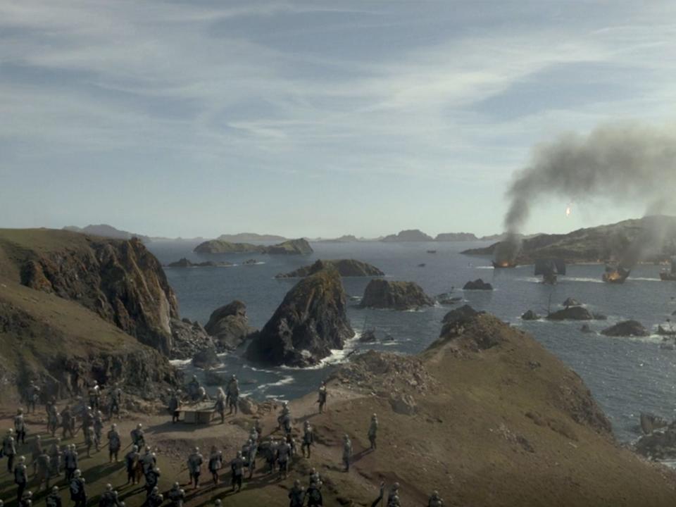 A scene from "House of the Dragon," showing a war camp near the edge of a cliff overlooking a naval battle.