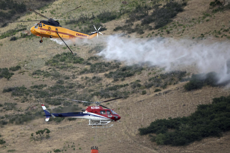 Two helicopters pass while fighting a wildfire in Springville on Monday, Aug. 1, 2022. A Utah man has been arrested on accusations he started a wildfire while trying to burn a spider with his lighter. A probable cause statement says 26-year-old Cory Allan Martin told deputies that he spotted the spider Monday while he was in a hiking area in the foothills south of Salt Lake City near the city of Springville. (Kristin Murphy/The Deseret News via AP)