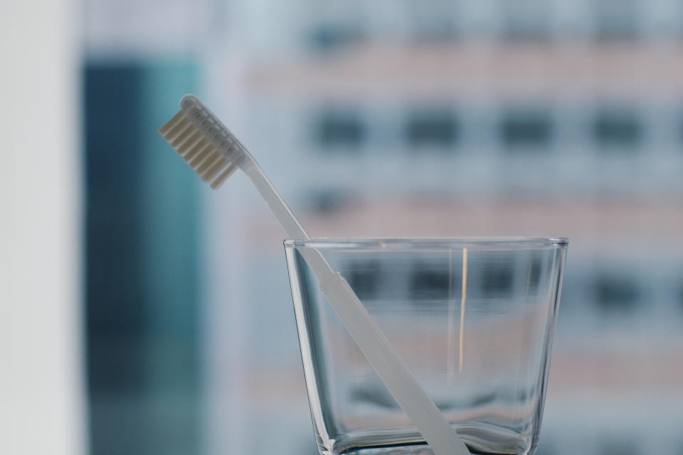 A single toothbrush stands upright in a clear glass with a blurry background