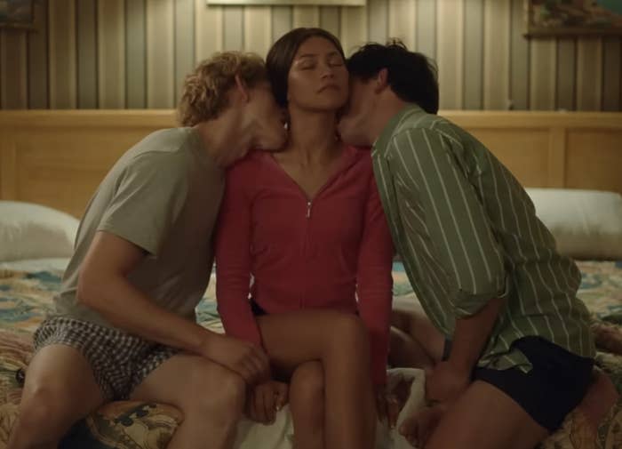 The image is a still from the "Challengers" movie trailer showing three people in a close moment on a bed, likely from a scene in the film