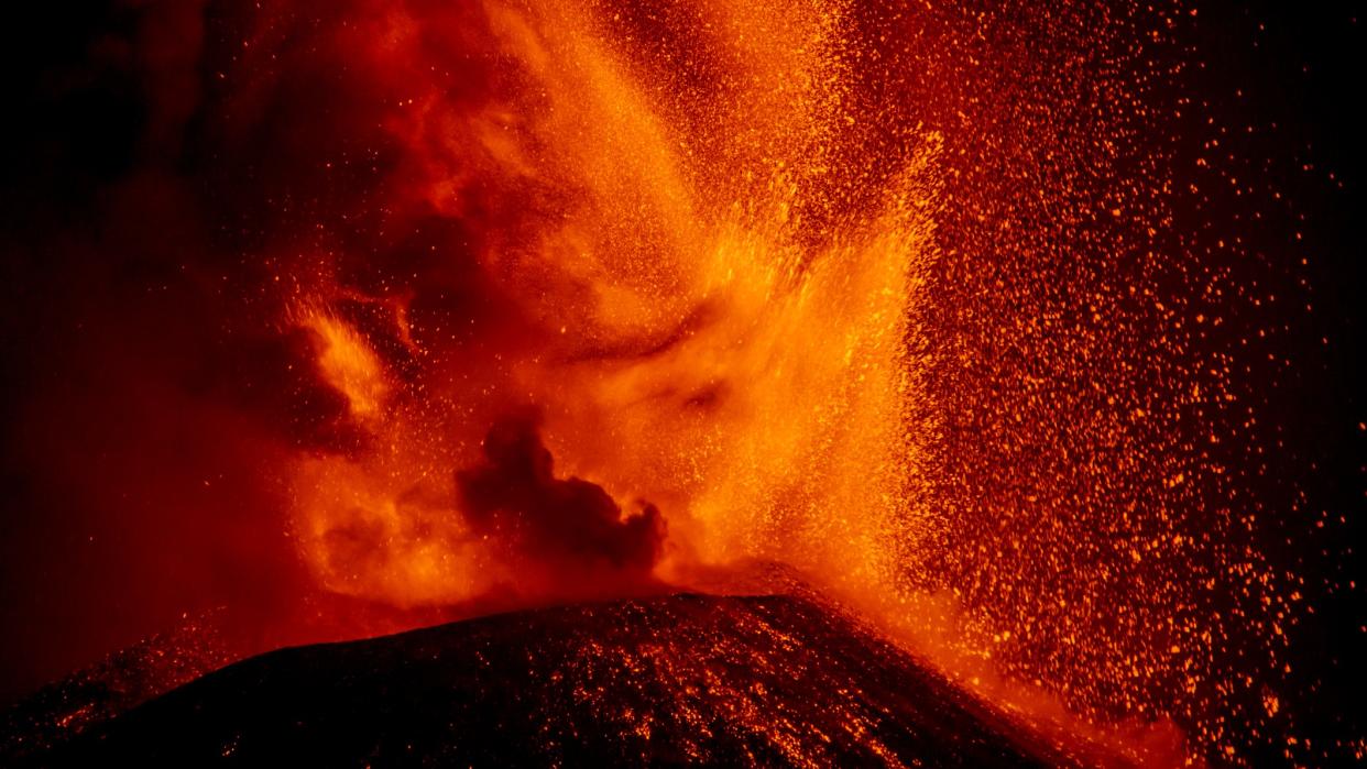  Lava erupts from a volcano in a huge shower of red molten rock. 