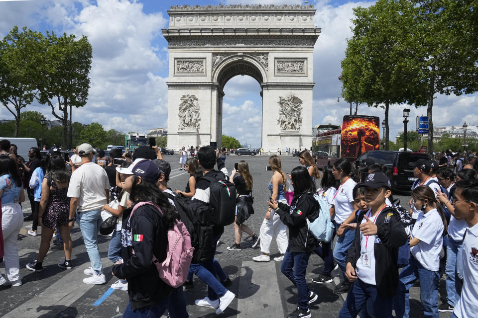 Tourists cross the Champs-Elysees avenue with the Arc de Triomphe in background, Thursday, July 6, 2023 in Paris. French government officials met with representatives of the tourism industry to discuss repercussions of unrest sparked by the police killing of a 17-year-old boy on tourist activity and on France's international image. The shooting death of Nahel Merzouk, who was of north African descent, prompted nationwide anger over police tactics and entrenched discrimination against people in low-income neighborhoods around France where many trace their roots to former French colonies. (AP Photo/Michel Euler)