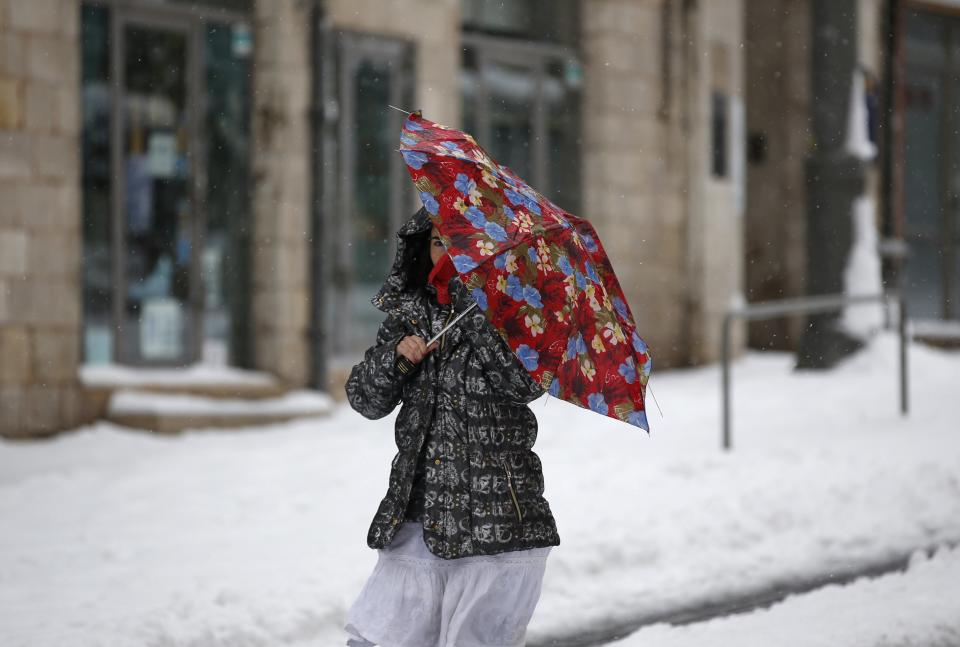 A woman walks through snow near Jerusalem's Old City December 14, 2013. Jerusalem's heaviest snow for 50 years forced Israeli authorities to lift a Jewish sabbath public transport ban on Saturday and allow trains out of the city where highways were shut to traffic. REUTERS/Darren Whiteside (JERUSALEM - Tags: ENVIRONMENT)