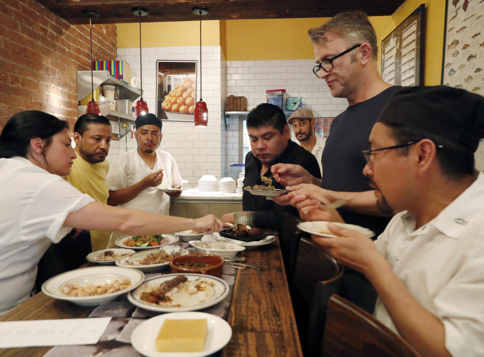 In this June 18, 2019, photo, Diaa Alhanoun, third from right, rear, watches as his co-chefs, restaurant manager and restaurant staff sample the Middle Eastern meal he prepared for dinner guests at Porsena, an Italian restaurant in the East Village, in New York, as part of the Refugee Food Festival. Offered for one night only at Porsena and other restaurants in the city, the food festival promotes acceptance of refugees in their host countries. Chef Lauren Radel, who helped curate the meal, is shown, far left joined by co-chef Alfredo Medel, far right. Restaurant manager Ian McRae, samples the food, second right. (AP Photo/Kathy Willens)