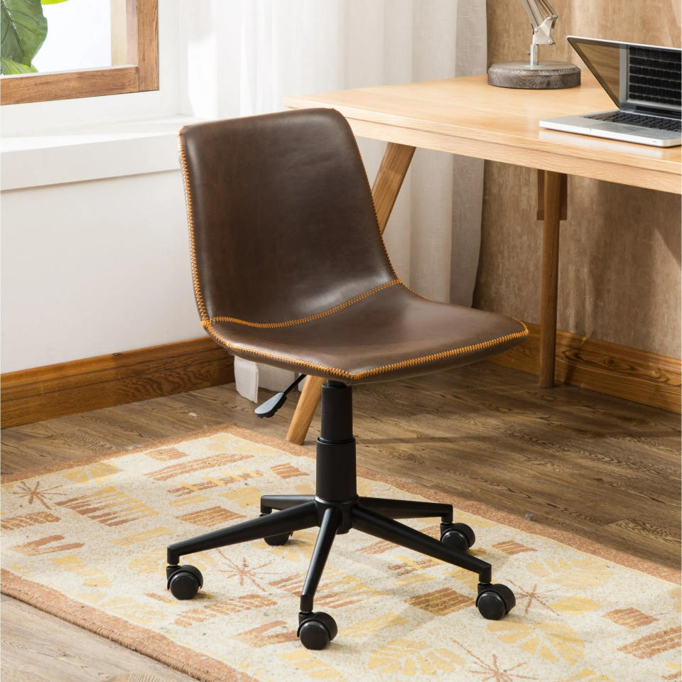 antique brown leather office chair with adjustable height and wheels, placed next to a wooden desk with a laptop and books on it, in a home office setting