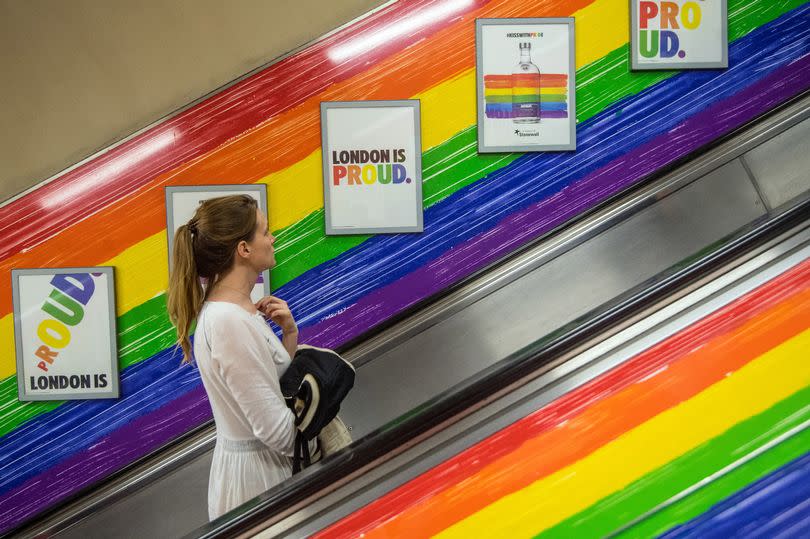 A woman rides a tube escalator decorated with the Pride flag colours