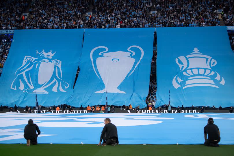 Manchester City fans unveil a banner with the three trophies from their treble winning season