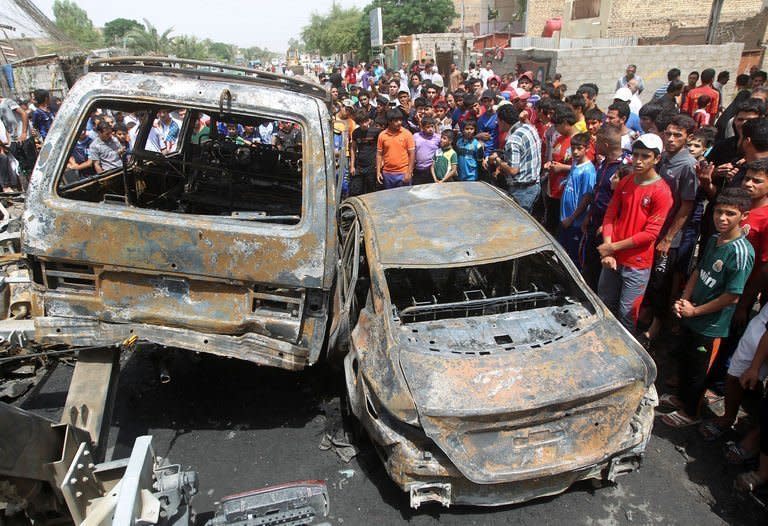 Iraqis gather around burnt vehicles at the site of a car bombing at a market in Baghdad's impoverished district of Sadr City, on May 16, 2013