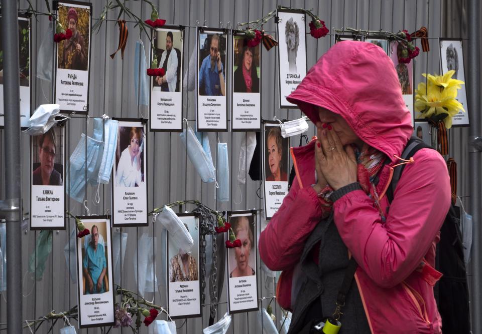 In this Wednesday, May 20, 2020 photo, a woman reacts as she walks past portraits of St. Petersburg's medical workers who died from coronavirus infected during their work, hanging at a unofficial memorial in front of the local health department in St.Petersburg, Russia. Russian health officials say more than 70 medical workers have died of coronavirus since the beginning of the outbreak. Health care workers believe the number to be much higher and they have compiled a list of more than 240. (AP Photo/Dmitri Lovetsky)