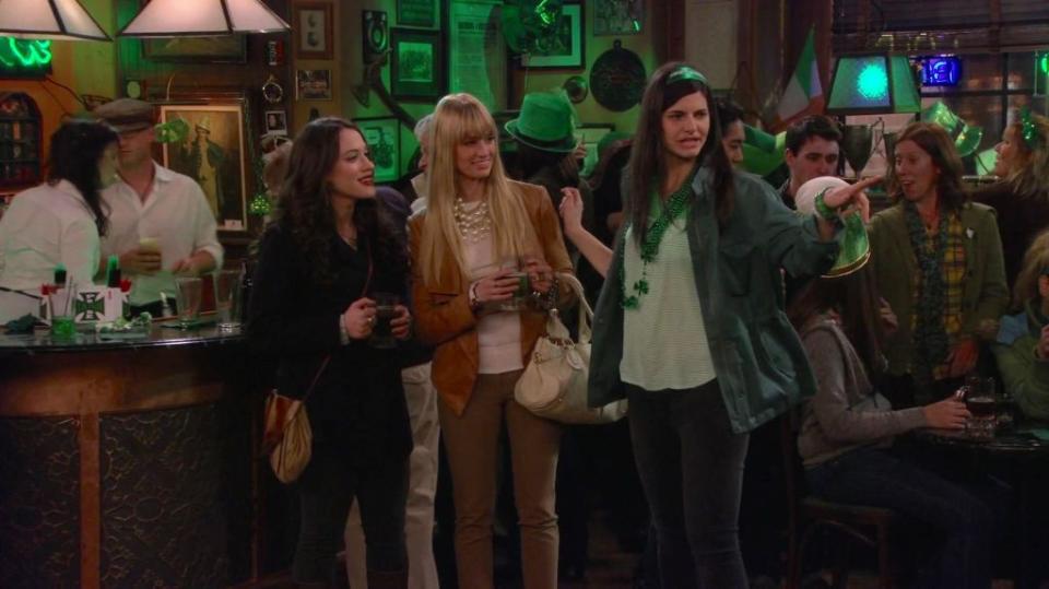 Max Black (Kat Dennings, from left) tries to get roommate and co-worker Caroline Channing (Beth Behrs) on board with a St. Patrick’s Day party parade with Monica (Lindsey Kraft). TBS