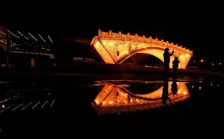 People take pictures in front of a "Golden Bridge on Silk Road" installation, set up ahead of the Belt and Road Forum, outside the National Convention Centre in Beijing, China May 11, 2017. Picture taken May 11, 2017. REUTERS/Stringer