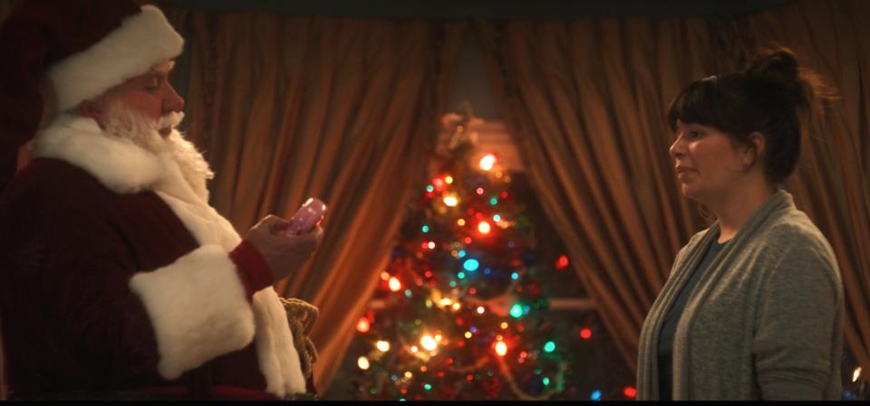 Santa Claus holds up a Polly Pocket toy while Casey's character, in a cardigan, watches him. There is a decorated Christmas tree in the background