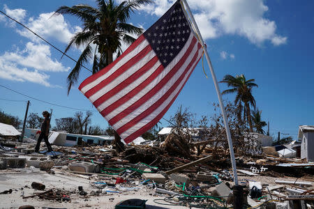 A resident carries belongings next to a U.S. flag in a debris field of former houses following Hurricane Irma in Islamorada, Florida, U.S., September 15, 2017. REUTERS/Carlo Allegri