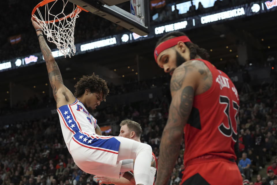 Philadelphia 76ers' Kelly Oubre Jr. hangs from the rim, near Toronto Raptors' Gary Trent Jr. during the second half of an NBA basketball game Saturday, Oct. 28, 2023, in Toronto. (Chris Young/The Canadian Press via AP)