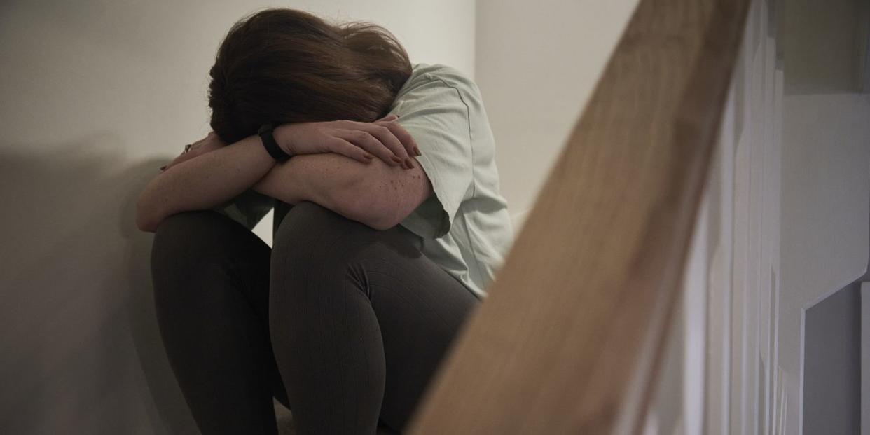 a woman suffering from depression or domestic abuse sat on the stairs of her home hiding her face