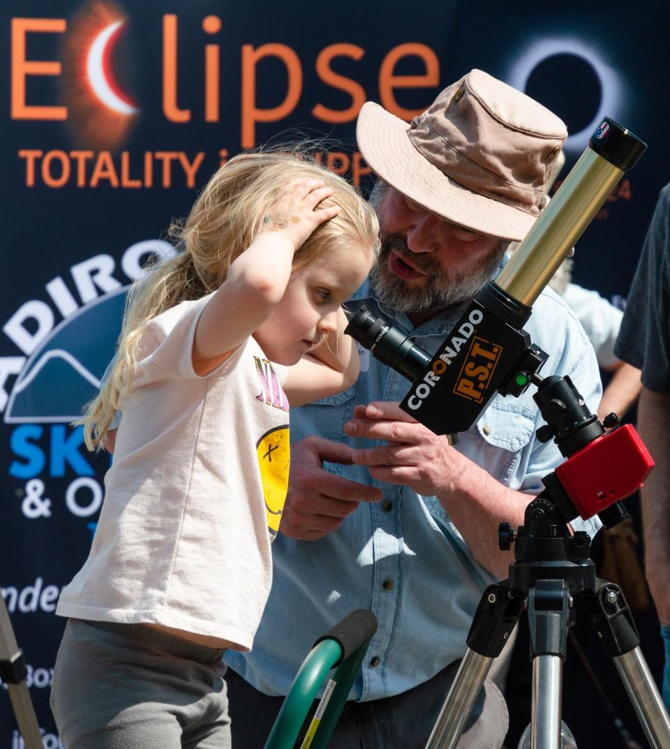 Seth McGowan of the Adirondack Sky Center in Tupper Lake, N.Y., shows a child how to look through a telescope. The center will host a community event for the April 8 solar eclipse.