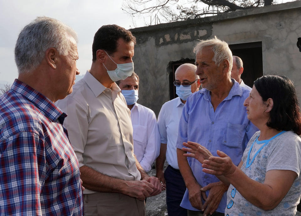 In this photo released Tuesday, Oct. 13, 2020 on the official Facebook page of the Syrian Presidency, Syrian President Bashar Assad, second from left, wearing a mask to help prevent the spread of the coronavirus, speaks with people during his visit to the coastal province of Latakia, Syria. Assad made a rare public visit to Latakia where he toured areas that suffered heavy damage in last week’s deadly wildfires. (Syrian Presidency via Facebook via AP)