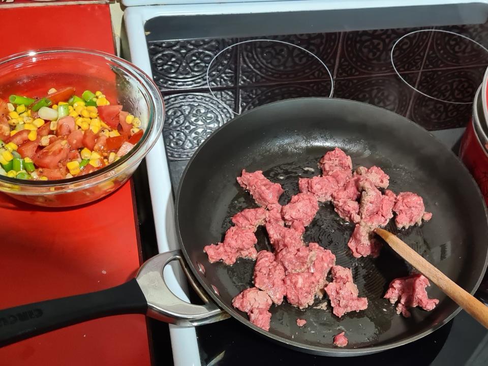 view of meat cooking on a stove with a bowl of vegetables on the side