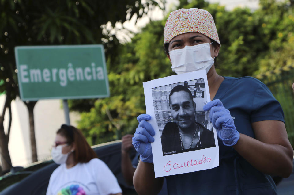 A health worker holds a photo of a person he said was his colleague who died of COVID-19, at a protest outside "Pronto Socorro 28 de Agosto" Hospital in Manaus, Brazil, Monday, April 27, 2020. Cases of the new coronavirus are overwhelming hospitals, morgues and cemeteries across Brazil as Latin America's largest nation veers closer to becoming one of the world's pandemic hot spots. (AP Photo/Edmar Barros)