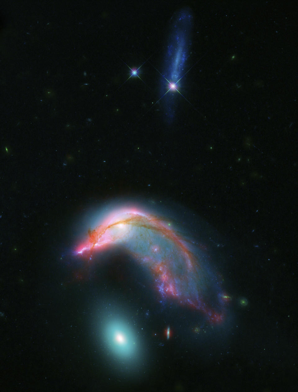 This image made available by NASA shows the interacting galaxies, NGC 2336, center, and NGC 2937, bottom, known collectively as Arp 142, as their mutual gravitational attraction slowly pulls them closer together. Data from NASA's Spitzer and Hubble space telescopes were combined to show light that spans the visible and infrared parts of the spectrum. The blue streak at the top of the image is an unrelated background galaxy that is farther away than Arp 142. (NASA-ESA/STScI/AURA/JPL-Caltech via AP)