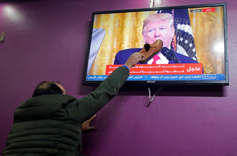 A Palestinian man places a shoe on a television screen broadcasting the announcement of Mideast peace plan by U.S. President Donald Trump, in a coffee shop in Hebron in the Israeli-occupied West Bank