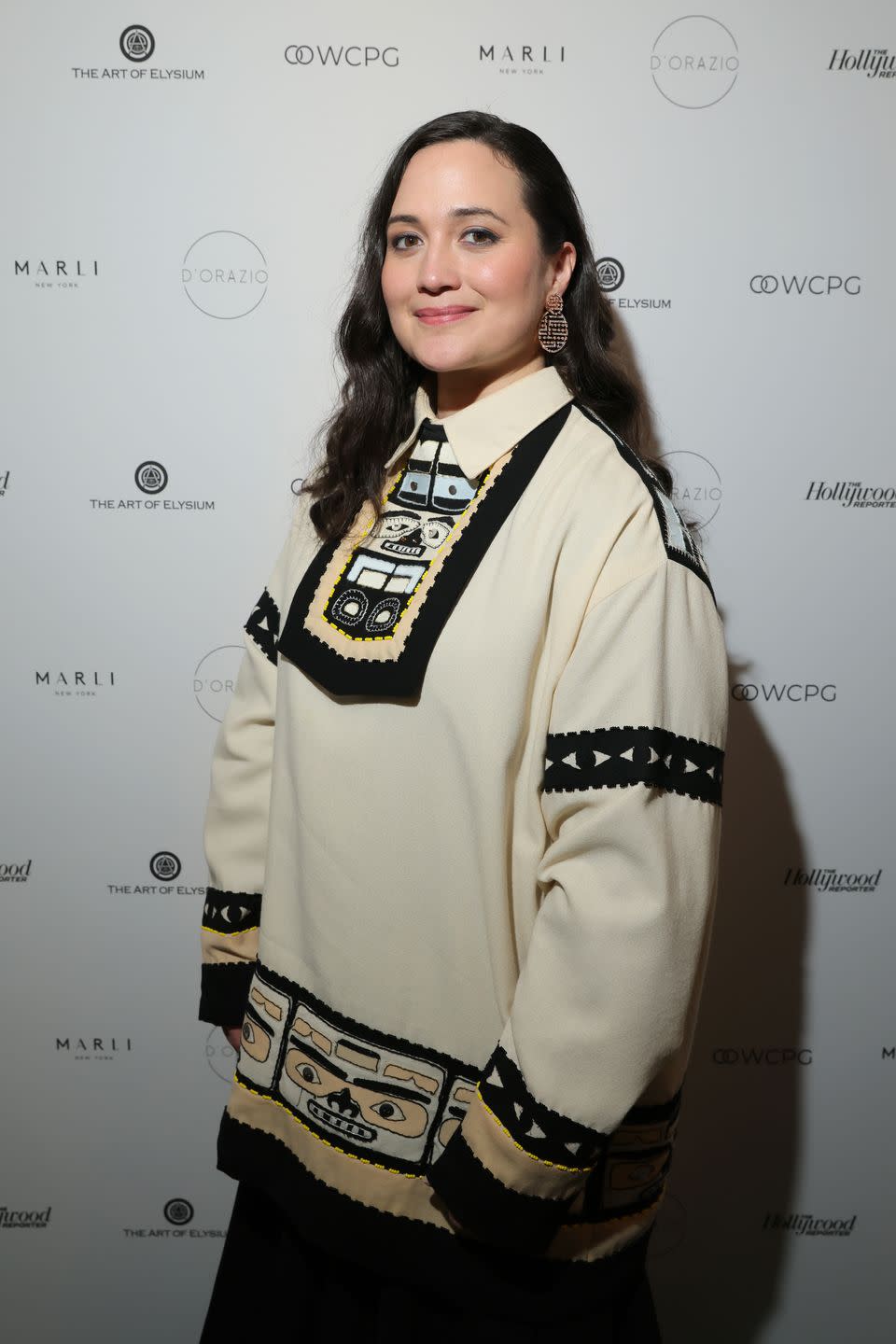 lily gladstone poses on the red carpet wearing a cream, collared jumper with embroidered motifs