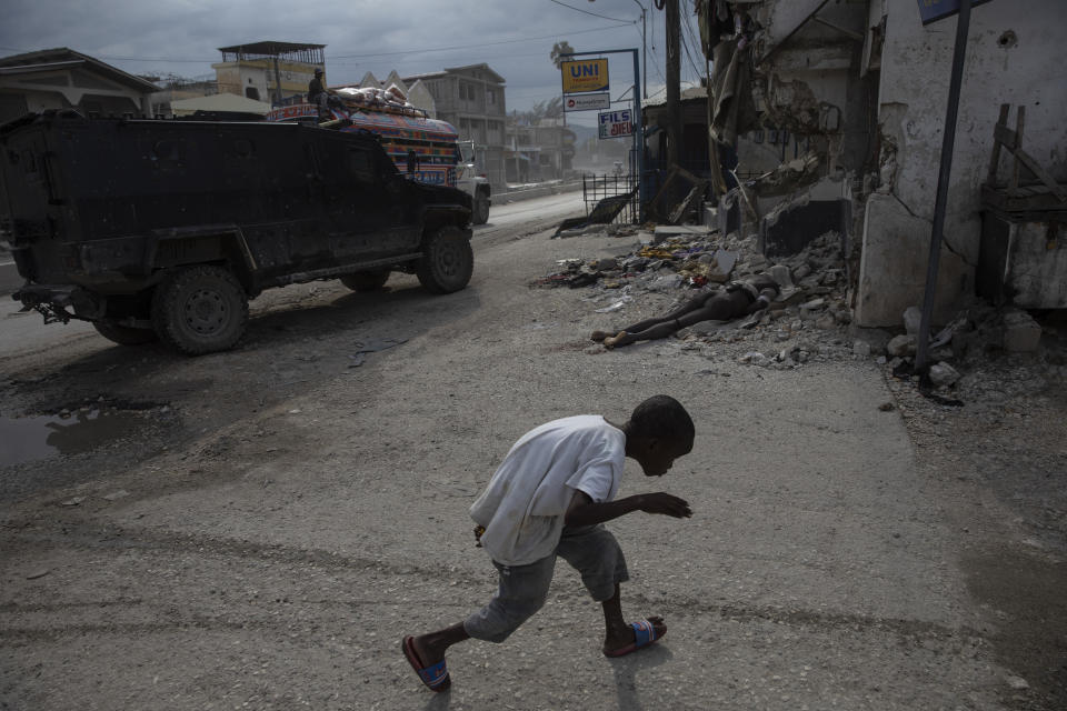 EDS NOTE: GRAPHIC CONTENT - FILE - A boy crouches to avoid the camera as he runs past the body of a man killed during clashes between police and gang members, in the Martissant neighborhood of Port-au-Prince, Haiti, Oct. 2, 2021. The violence in the Martissant neighborhood forced the aid group Doctors Without Borders in August to close an emergency clinic that had served the community for 15 years. (AP Photo/Rodrigo Abd, File)