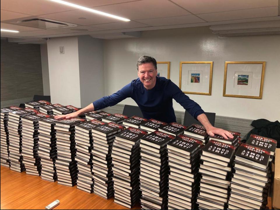 James Comey stands in front of a wall of signed books.