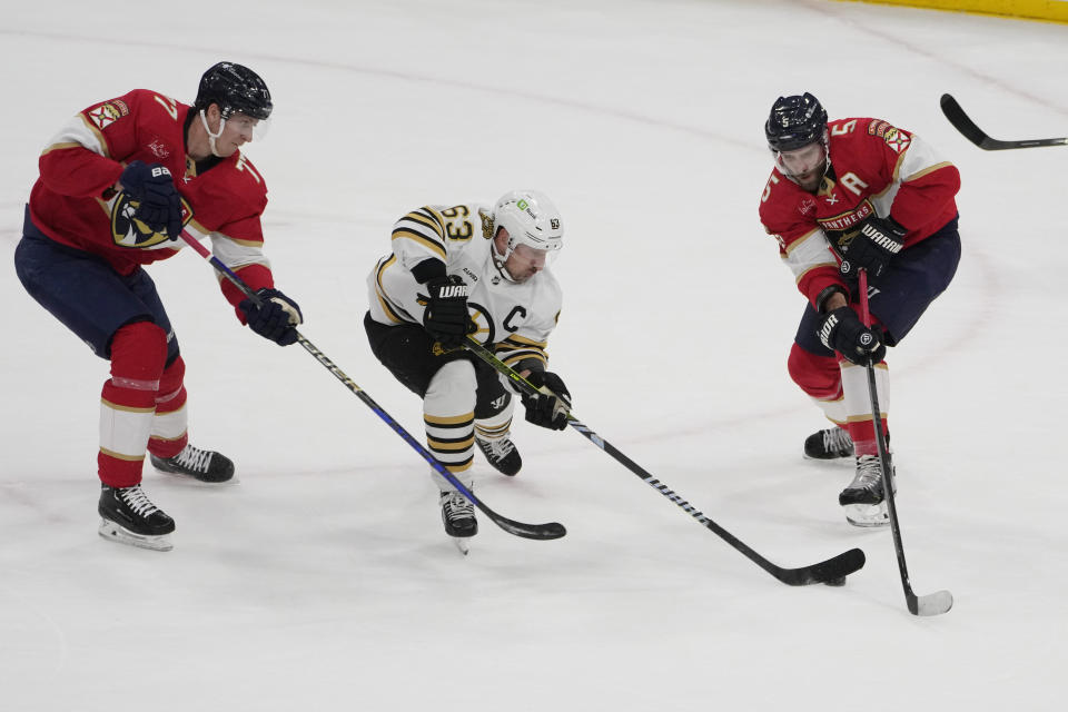 Boston Bruins left wing Brad Marchand (63) moves the puck as Florida Panthers defensemen Niko Mikkola (77) and Aaron Ekblad (5) defend during the first period of an NHL hockey game, Wednesday, Nov. 22, 2023, in Sunrise, Fla. (AP Photo/Marta Lavandier)