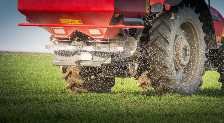 A tractor spreading fertilizer over a farm field.