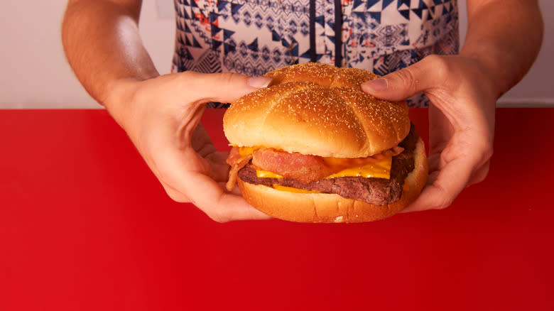 Hands holding Wendy's burger over red table