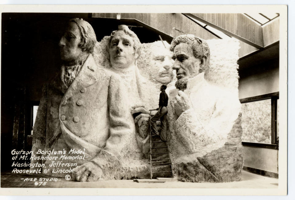 Sculptor Gutzon Borglum's model of Mt. Rushmore with Washington, Jefferson, Roosevelt, and Lincoln faces; artist standing beside it