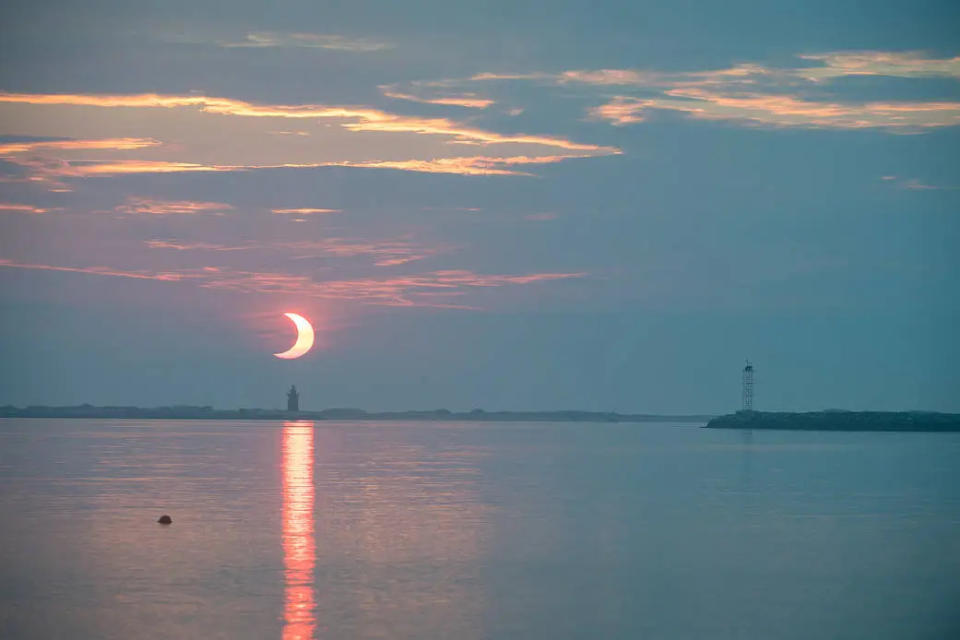 A partial solar eclipse is seen as the sun rises behind the Delaware Breakwater Lighthouse, Thursday, June 10, 2021, at Lewes Beach in Delaware. The full annular or “ring of fire” solar eclipse was visible to some parts of Greenland, Northern Russia, and Canada.