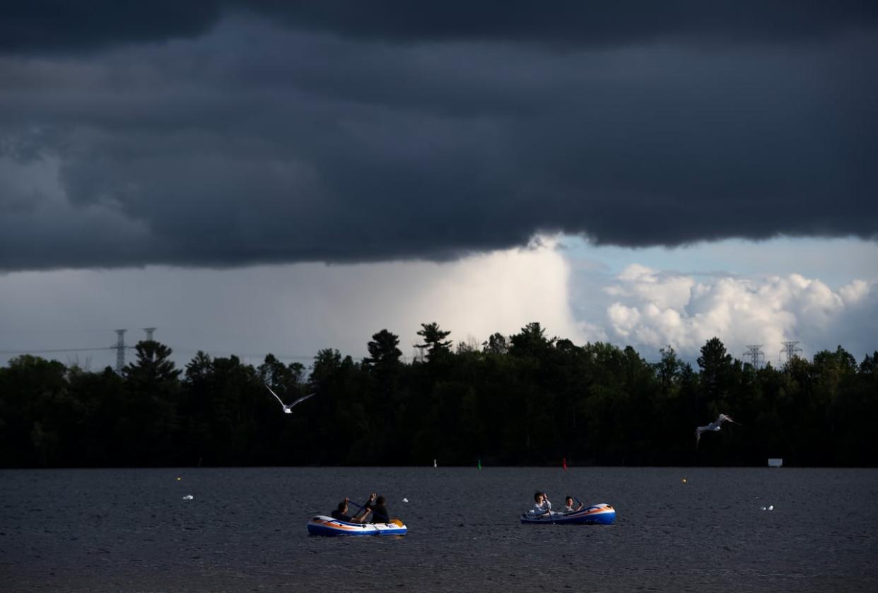 Storm clouds are seen in the distance as people paddle inflatable boats at Mooney's Bay in Ottawa in May 2020. Environment Canada has issued a severe thunderstorm watch for the Ottawa area on Tuesday. (Justin Tang/Canadian Press - image credit)