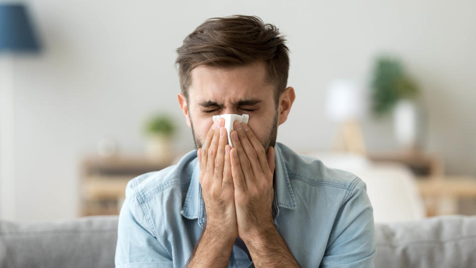 Man sneezing into tissue because his allergies have worsened after sleeping on a mattress infested with dust mites