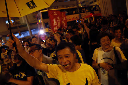 A protester holds a yellow umbrella, the symbol of the Occupy Central movement, in support of jailed Hong Kong student leaders Joshua Wong, Nathan Law and Alex Chow, while officers from the Correctional Services Department stand guard outside a prison in Hong Kong, China August 18, 2017. REUTERS/Tyrone Siu