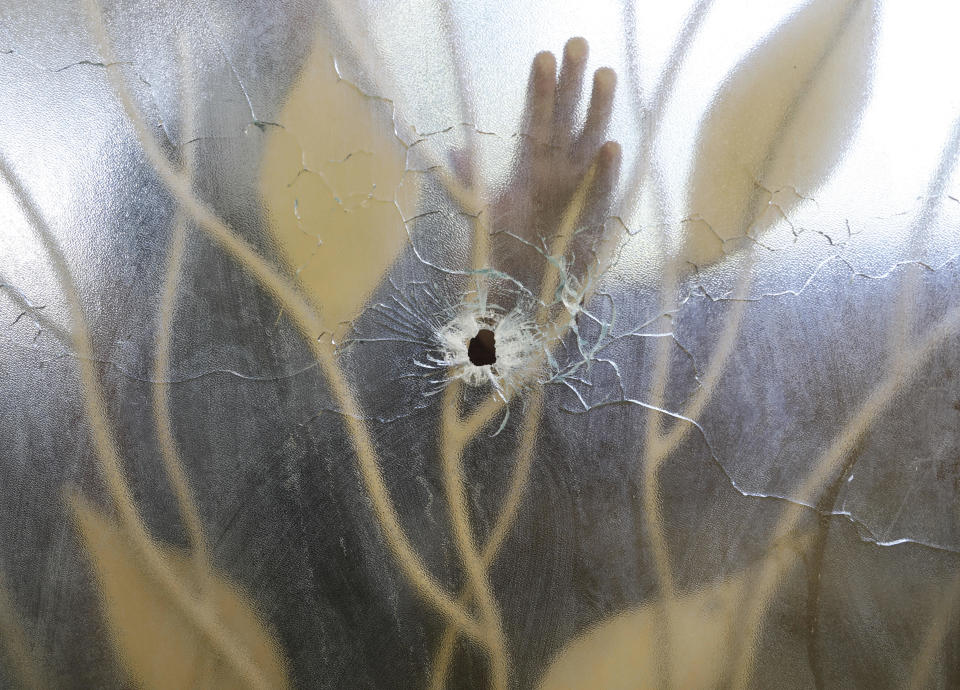 El trabajador de un hospital coloca la mano sobre una puerta de cristal de la clínica que fue perforada por un disparo durante el ataque del día anterior al Centro Hospitalario Fontaine, el jueves 16 de noviembre de 2023, en la zona de Cité Soleil, de Puerto Príncipe, Haití. (AP Foto/Odelyn Joseph)