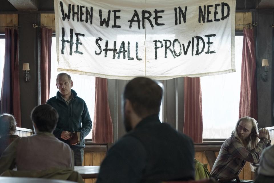 David stands in front of a big sign preaching to his followers on The Last of Us
