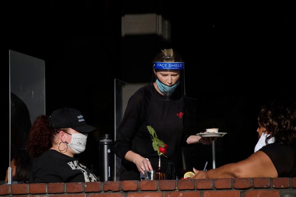 A waiter wearing personal protective equipment (PPE) serves customers dining outdoors in Manhattan Beach, California, November 21, 2020 a few hours before the start of the new 10:00 pm to 5:00 am curfew during increased Covid-19 restrictions. - The United States surpassed 12 million Covid-19 cases today, according to the Johns Hopkins University real-time tracker. (Photo by Patrick T. Fallon / AFP) (Photo by PATRICK T. FALLON/AFP via Getty Images)