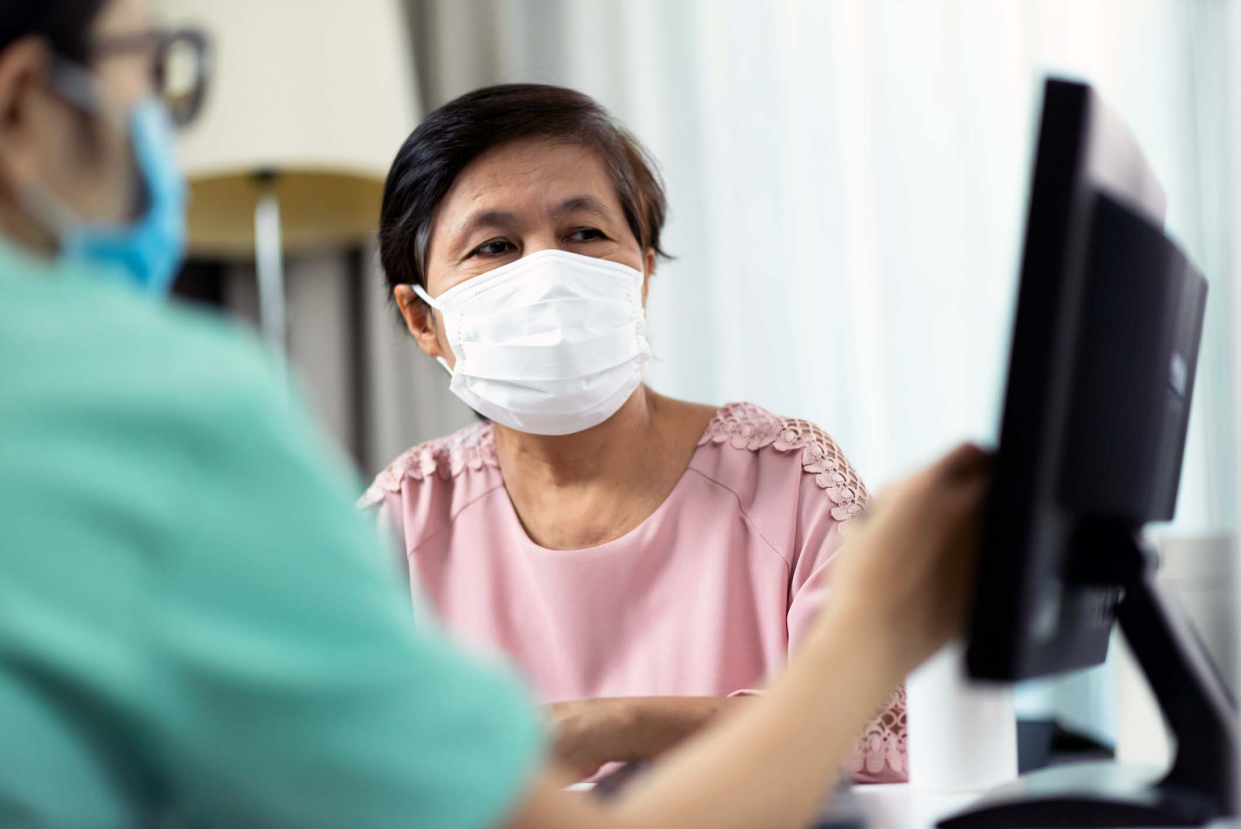 Asian Female Doctor or Nurse in green uniform talking giving advice to Elderly woman patient in pink cloth and looking to computer screen monitor together in medical room at the hospital