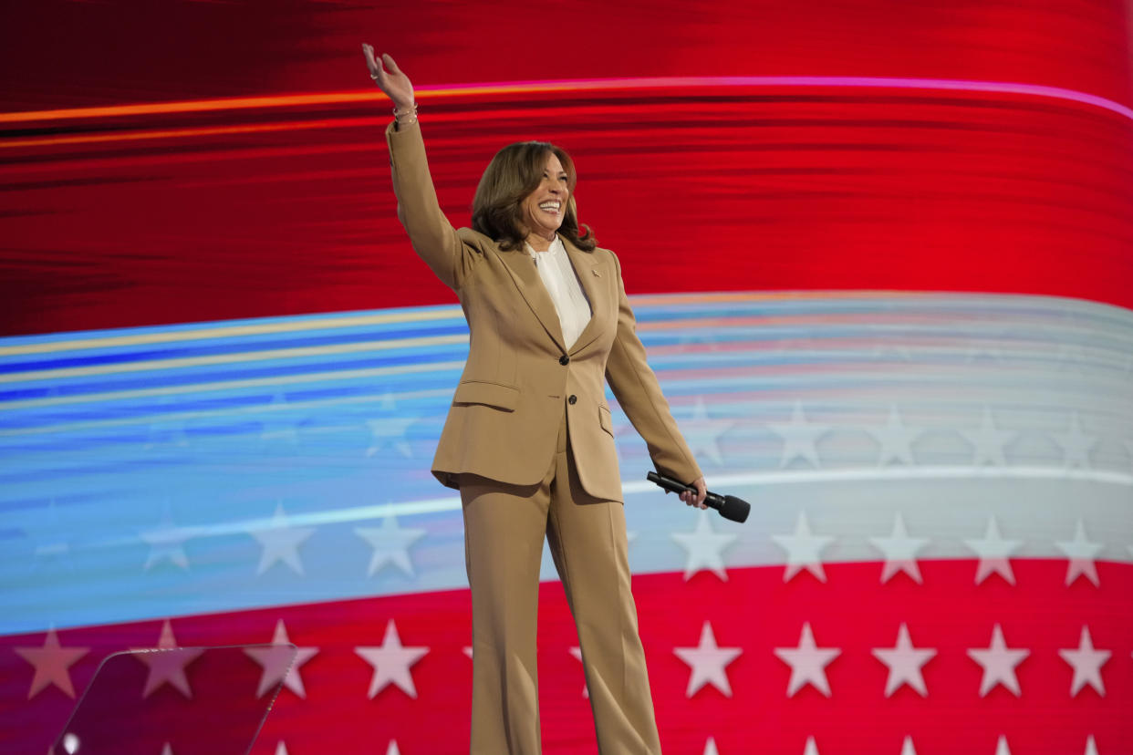 Vice President Kamala Harris, in full tan suit, waves onstage during the Democratic National Convention.