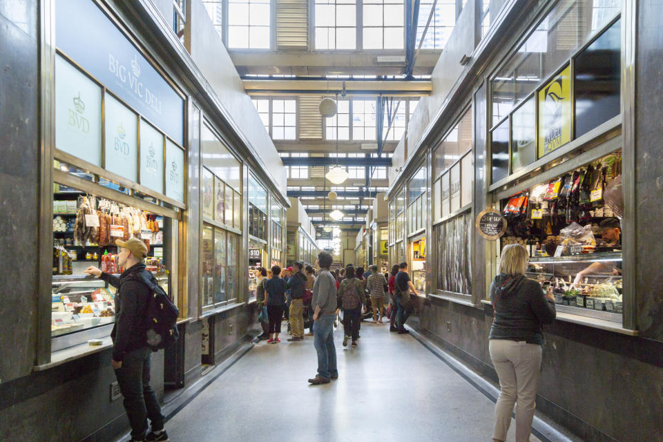 People browsing and shopping at various stalls inside a high-ceiling marketplace