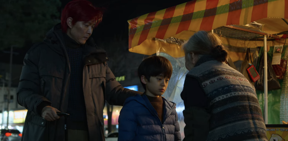 An elderly lady talking to a young boy, who's with Gi-hun