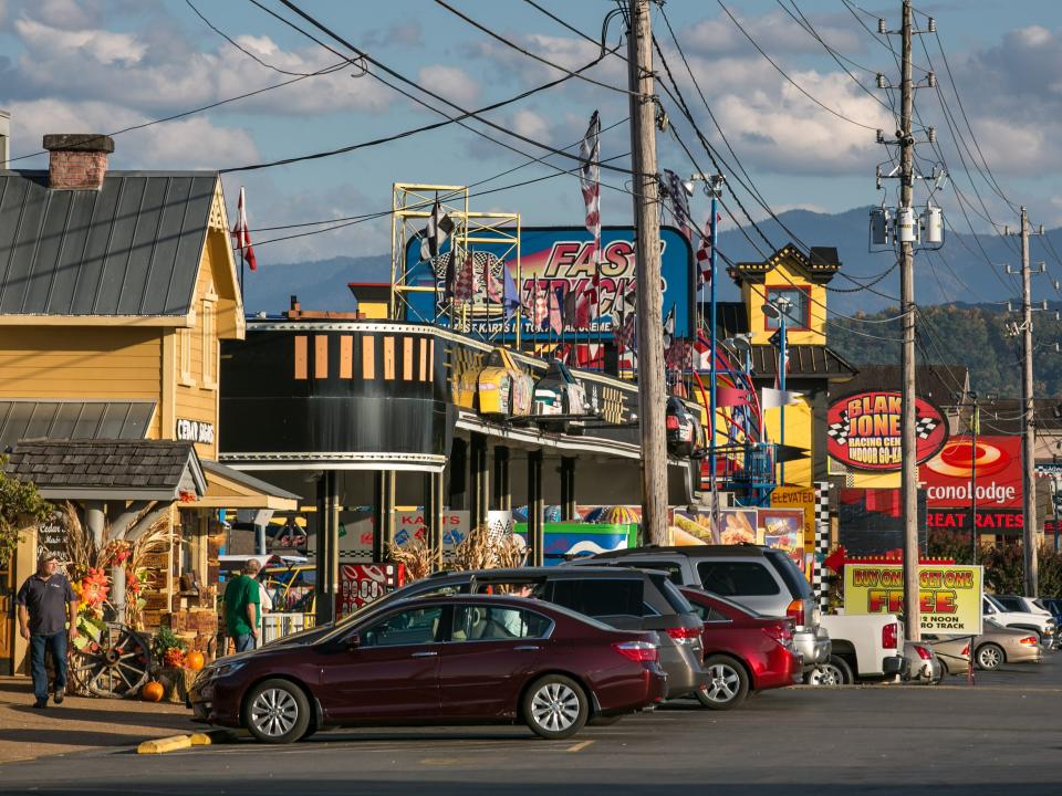 Shops and cars parked along The Parkway are viewed on October 18, 2016 in Pigeon Forge, Tennessee, with cloudy blue skies and mountains in the background.