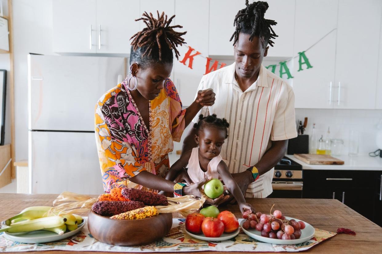 Black girl names can be unique, inspired by culture and the places you live. This list will help you find the perfect name for your new baby girl. Pictured: A Black family with a young baby girl who is reaching for an apple.