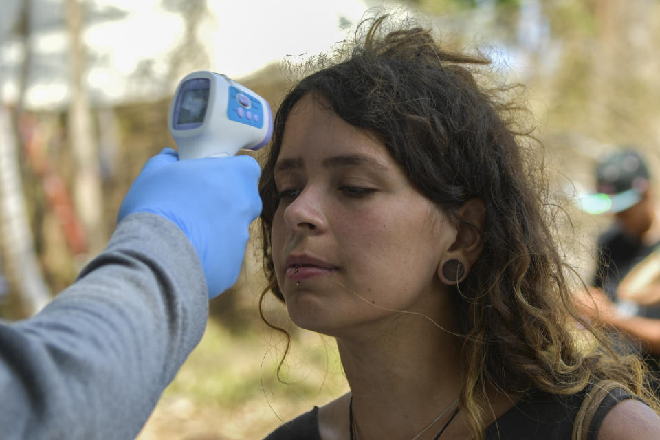 A Panama's health worker checks the temperature of an attendee of the Tribal Gathering festival rock in Cuango, Colon province, Panama, on March 18, 2020. - Hundreds of foreigners participating in a music festival in a remote Caribbean beach in Panama were placed under quarantine with no COVID-19 cases confirmed among them, after the festival was locked down. (Photo by Luis ACOSTA / AFP) (Photo by LUIS ACOSTA/AFP via Getty Images)